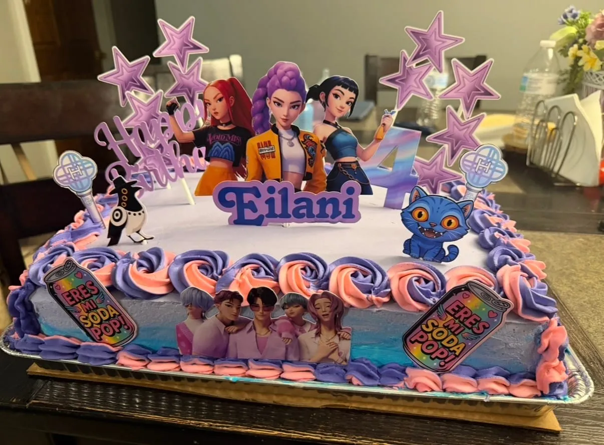 Kids' birthday sheet cake with superhero-girl figurine toppers and purple star picks over blue and white buttercream waves