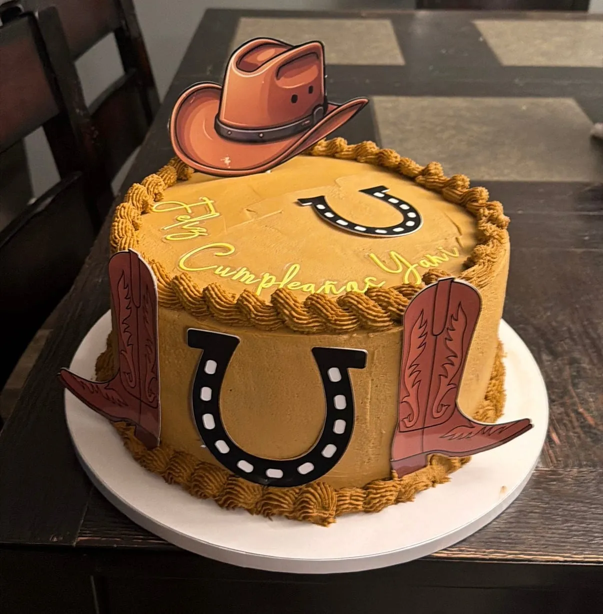 Western-themed cake with a cowboy hat topper, tooled-leather look, and a horseshoe on the front in tan buttercream