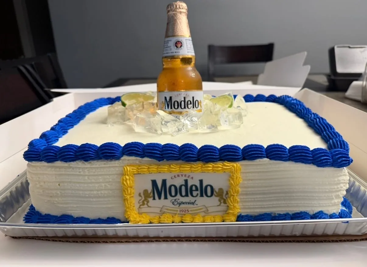 Sheet cake designed like a Modelo beer bucket, with blue and white piping and a bottle on top over crushed-ice sugar