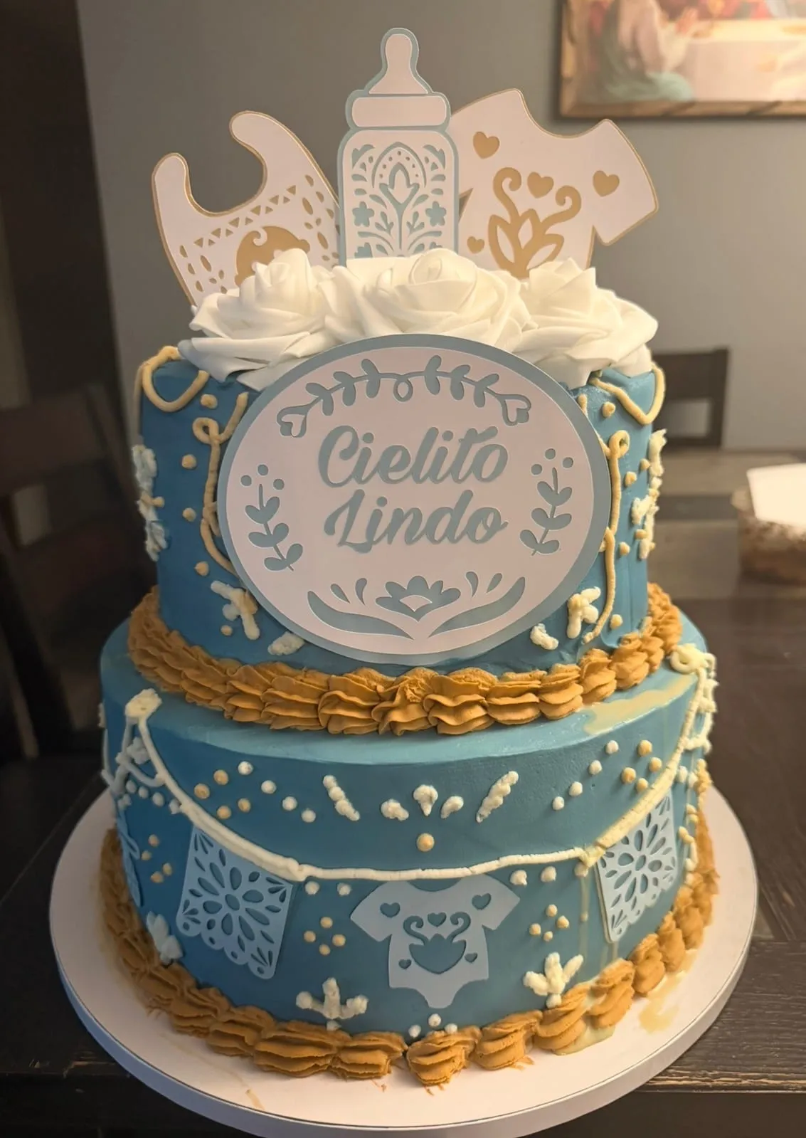 Two-tier blue and gold cake with a decorative 'Cielito Lindo' plaque and papel-picado toppers