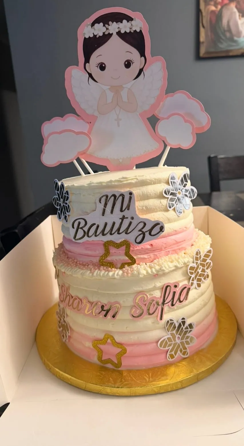 Baptism cake in pink and cream with a winged angel topper and a 'Mi Bautizo' plaque, finished with snow-like accents