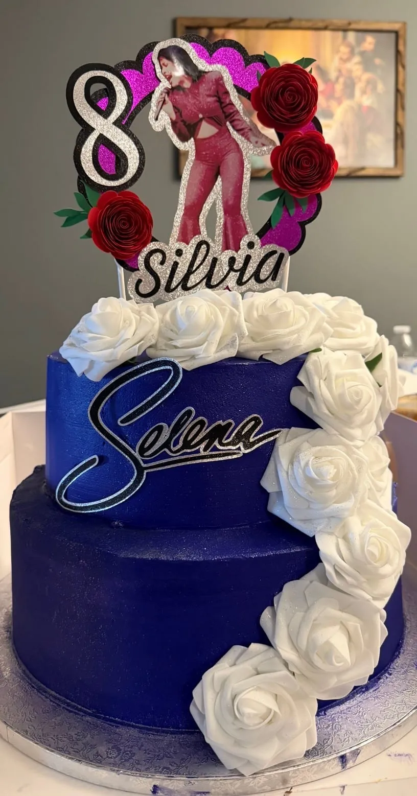 Royal-blue cake with white buttercream roses and a script name topper