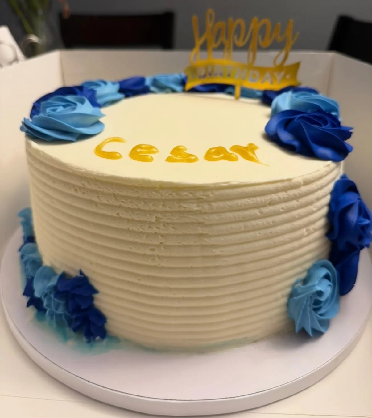 White and blue textured buttercream cake with gold script lettering and blue sugar roses