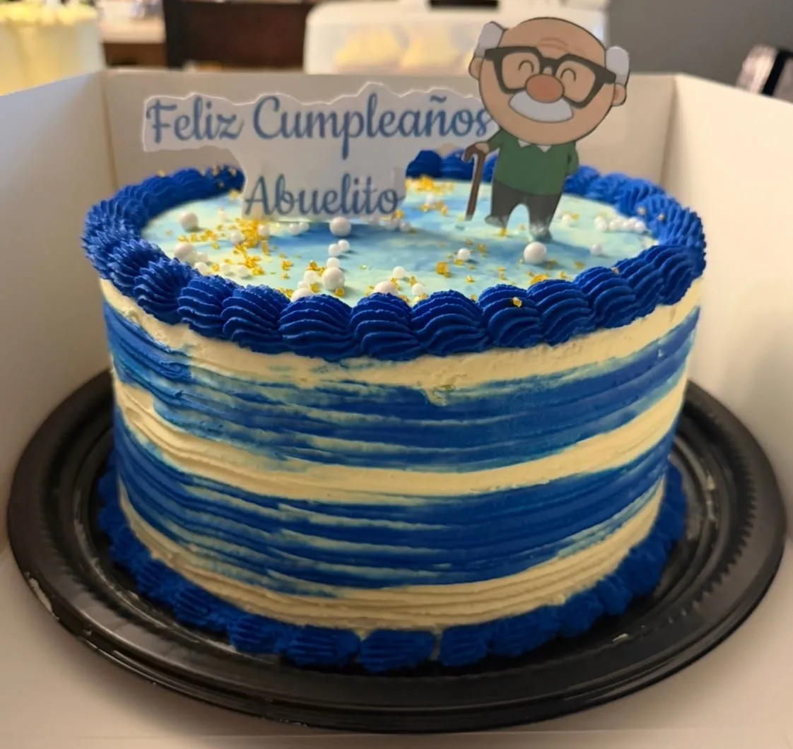 Blue-striped buttercream cake with a cartoon grandpa topper reading 'Feliz Cumpleaños Abuelito'
