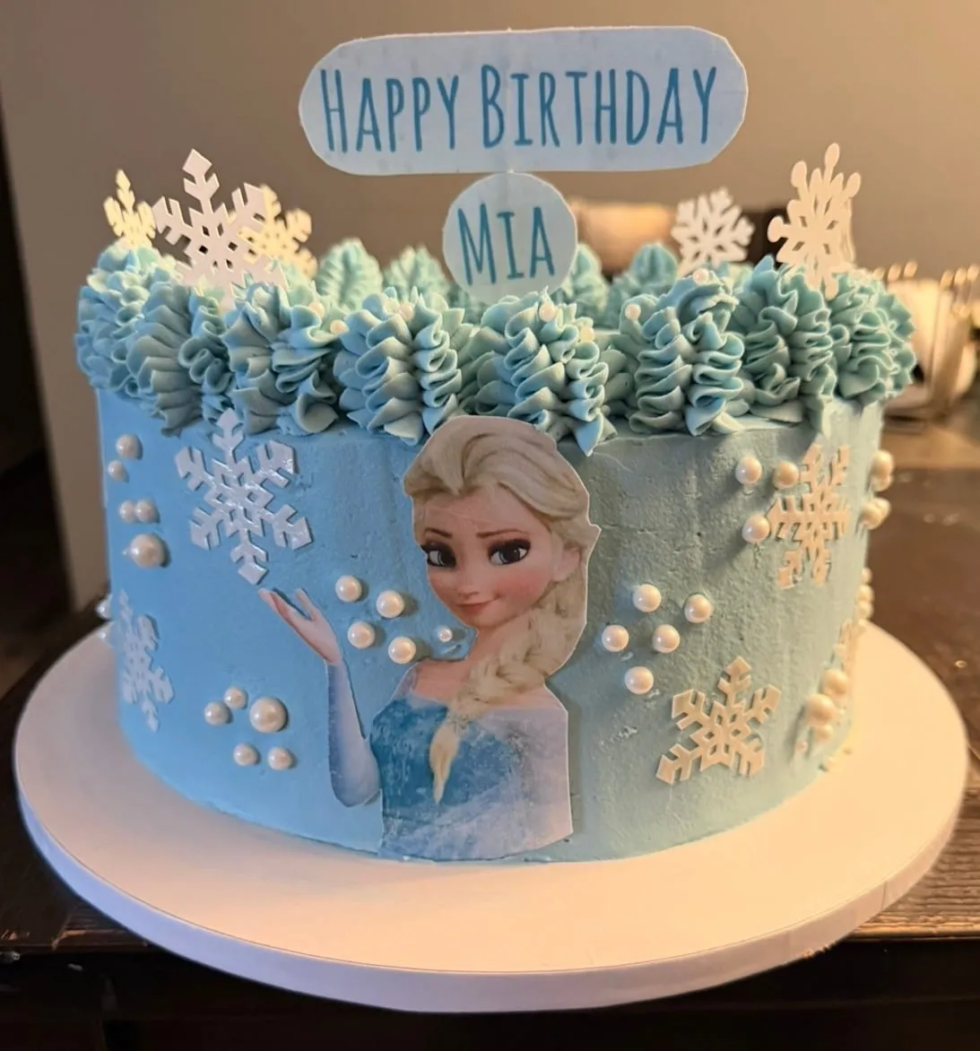 Frozen-themed cake with an Elsa edible image, blue snowdrift piping, and pearl snowflakes