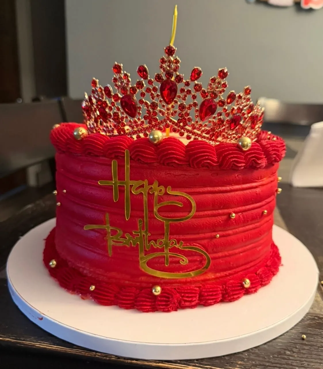 Deep-red cake with a jeweled crown topper and gold script lettering