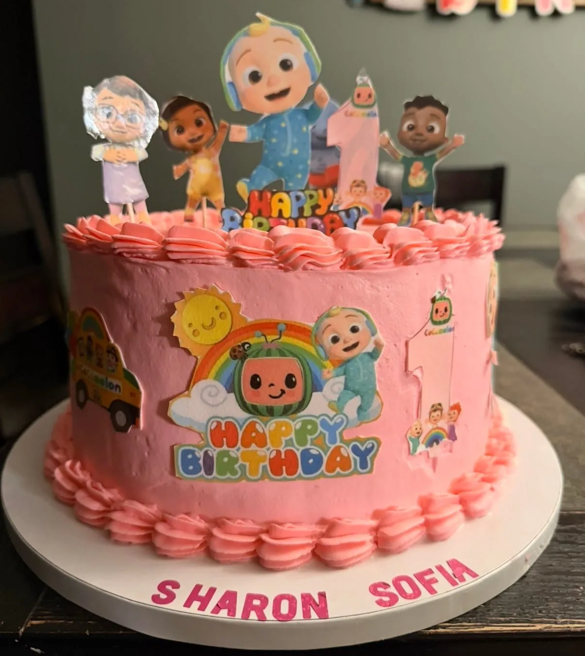 Cocomelon first-birthday cake in pink with character toppers and a number-one topper