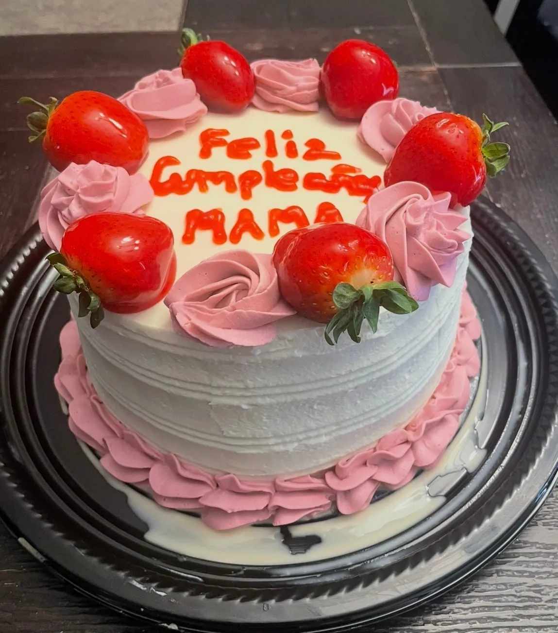White and pink cake ringed with fresh strawberries and red script lettering for 'Mamá'