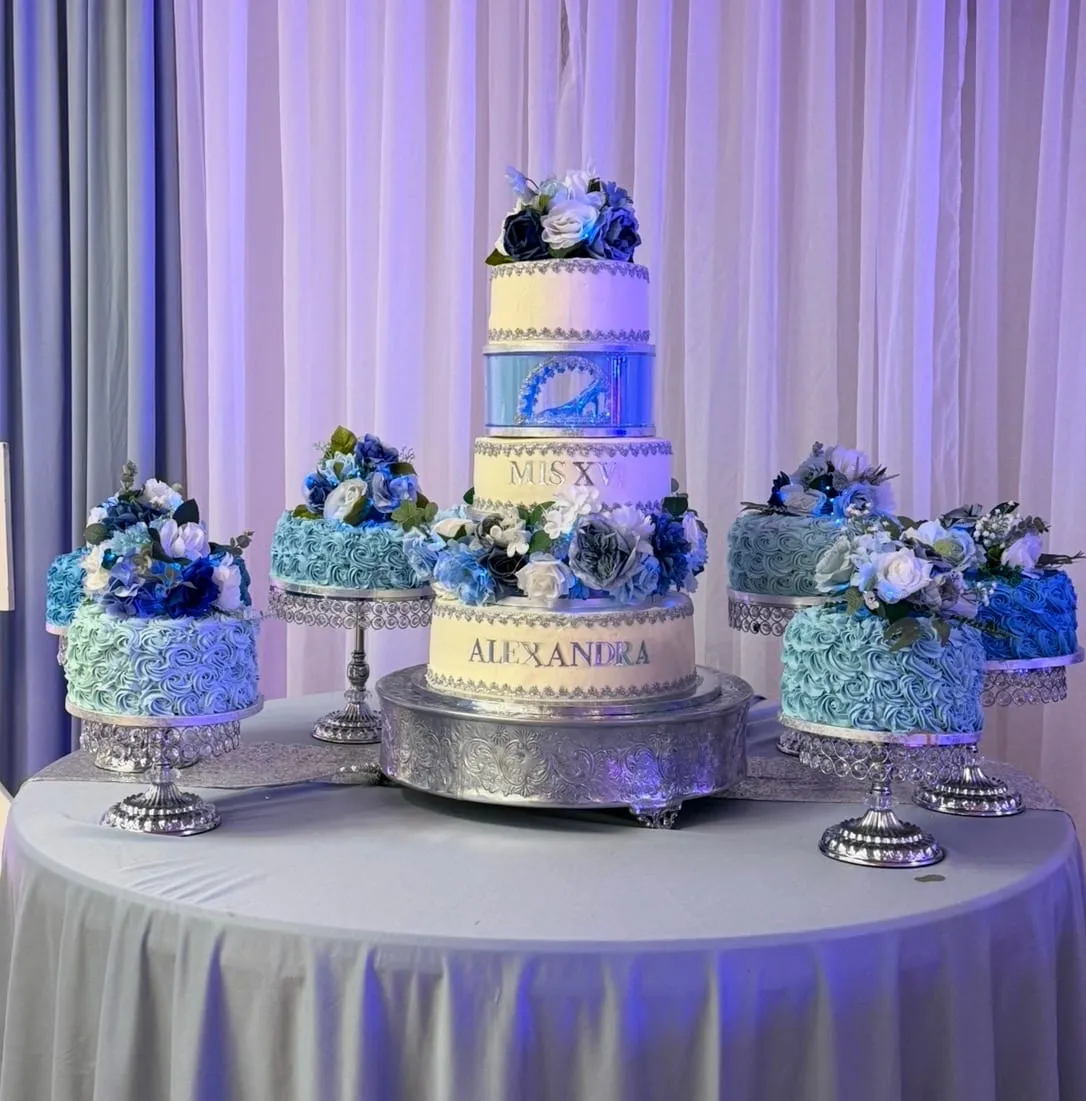 Quinceañera dessert table with a tiered blue and silver cake flanked by matching floral mini cakes