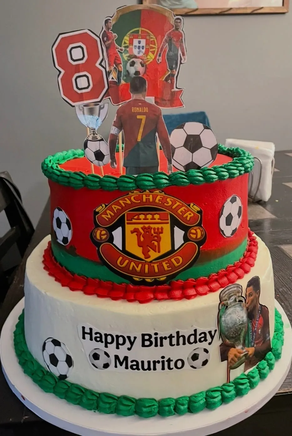 Two-tier Manchester United cake with team crest, soccer balls, a trophy, and a player figure