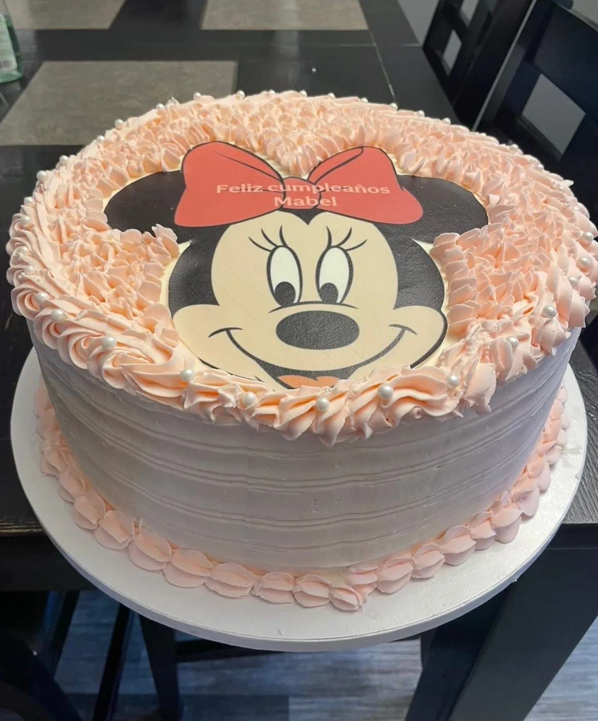Minnie Mouse cake in pink with a Minnie face edible image, a red bow, and ruffled buttercream